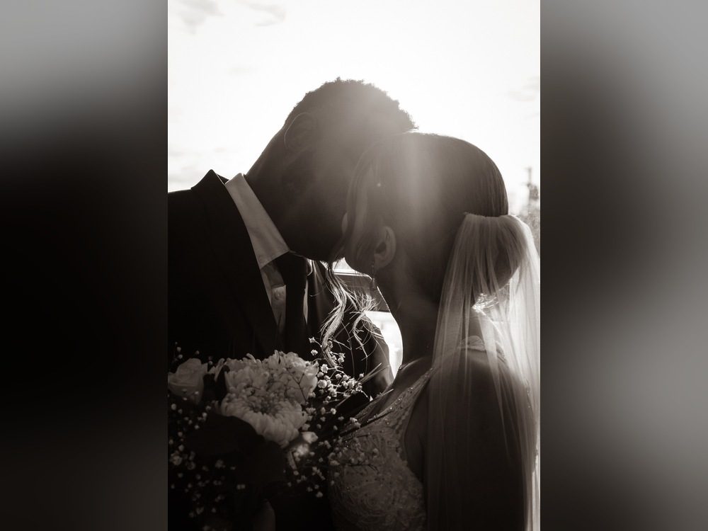 Backlit silhouette of a bride and groom kissing in black and white, with a bouquet in the foreground