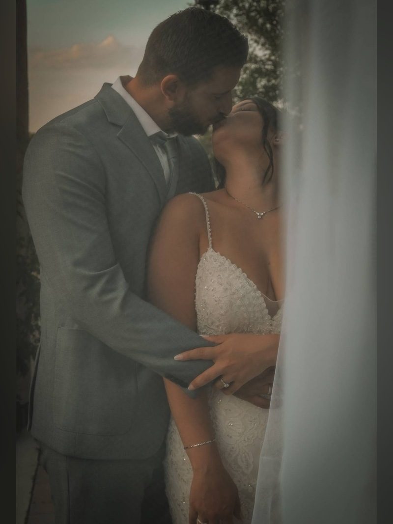Groom in a gray suit kissing the bride in a beaded gown, with her veil in the foreground