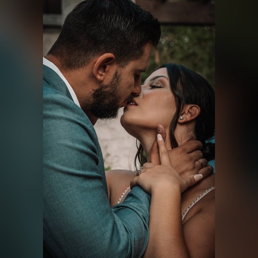 Close-up of a groom in a teal jacket kissing the bride, his hand on her neck