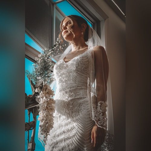 Bride in a lace wedding gown and veil looking up beside a bright blue window