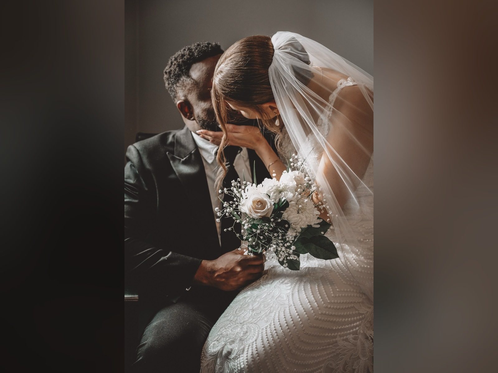 Bride in a veil with her hand on the groom's face, holding a white bouquet