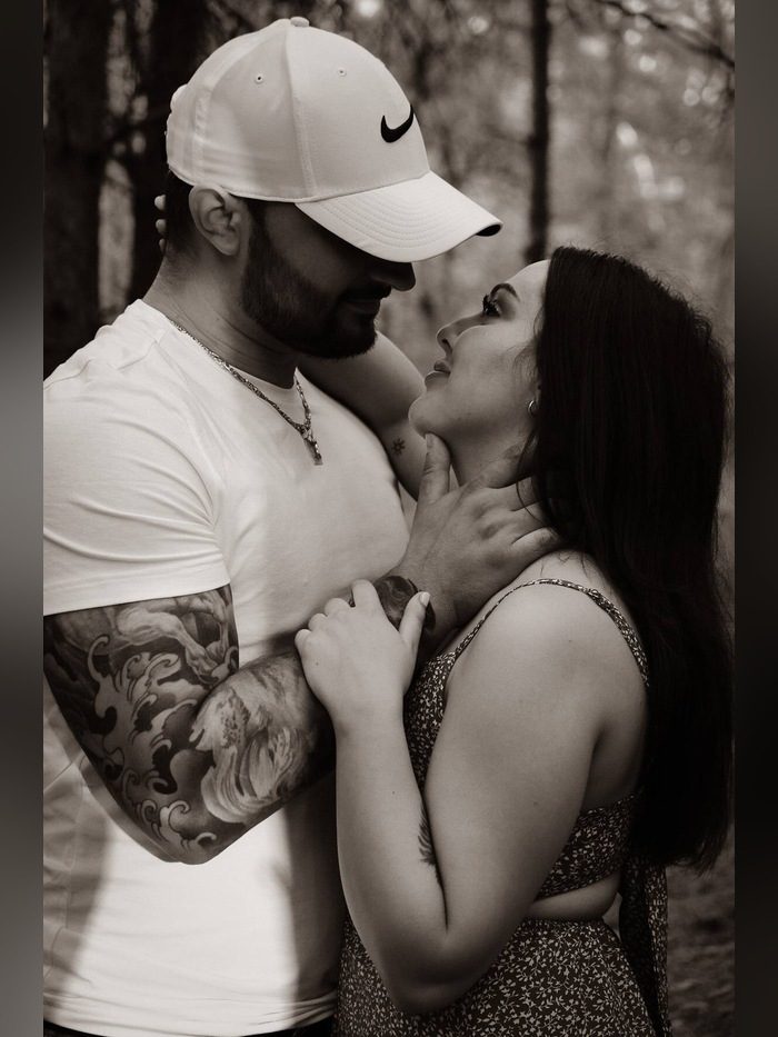 Couple embracing in a forest, the man in a white cap with a tattooed sleeve, black and white
