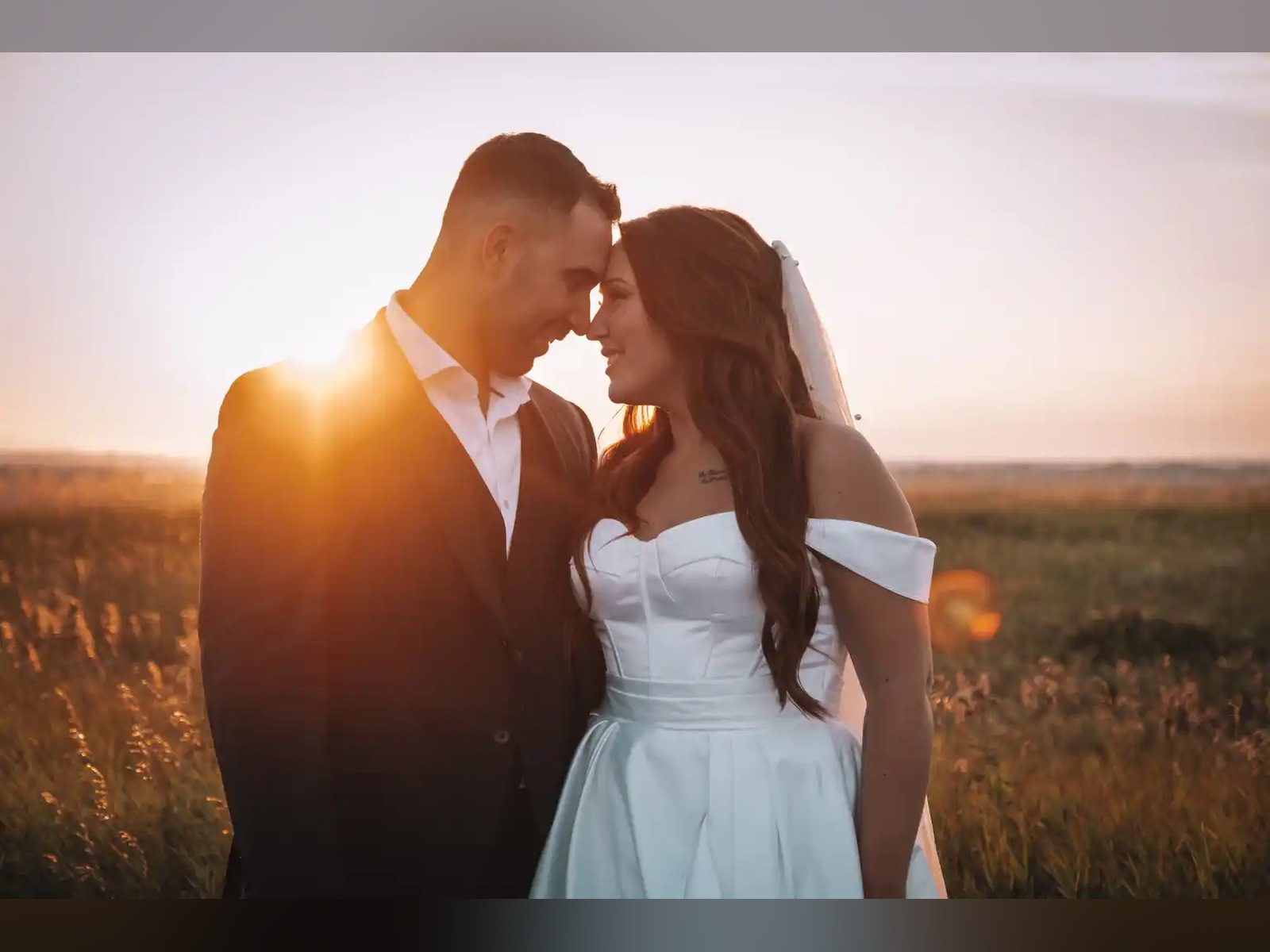 Bride and groom touching foreheads in a field at sunset